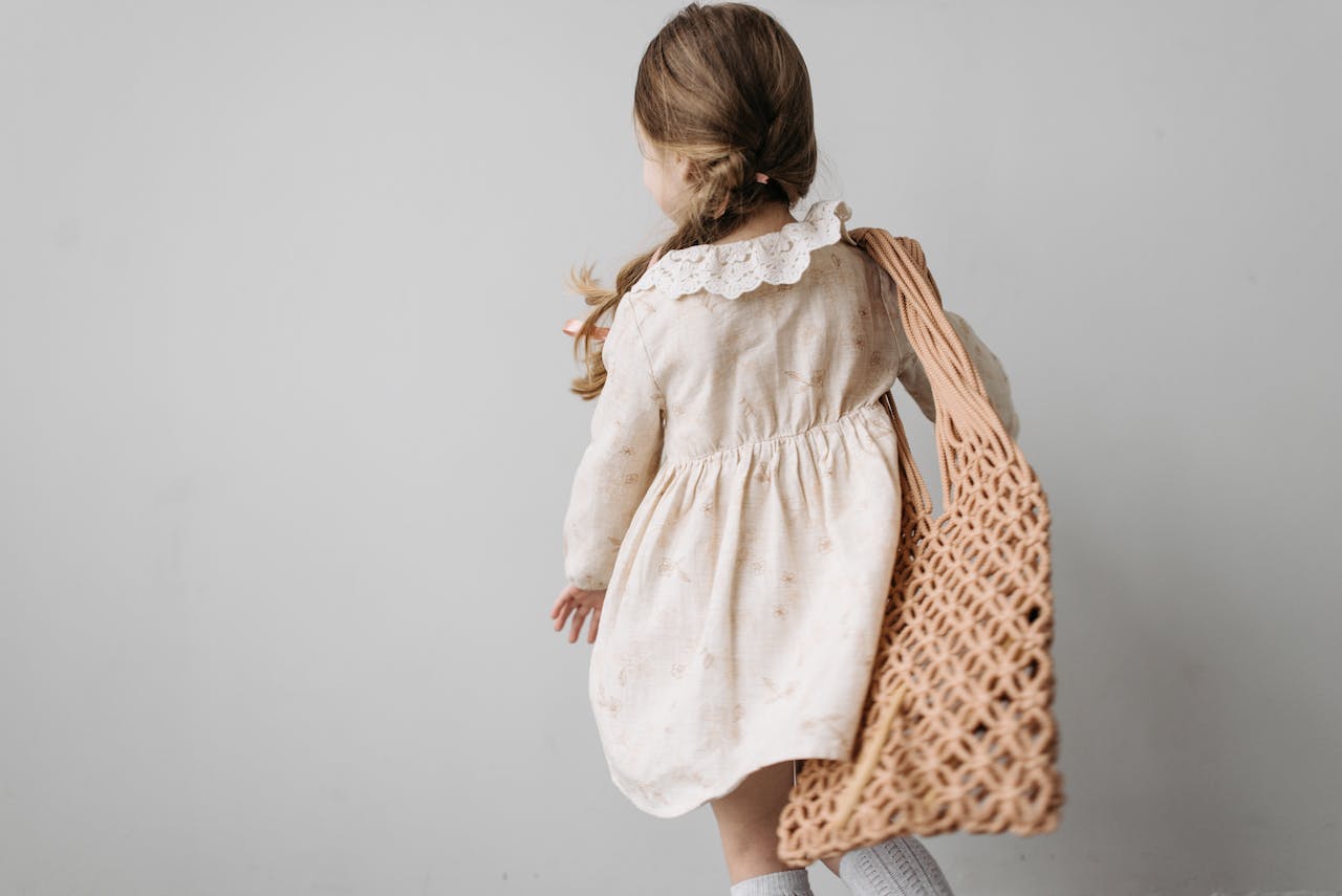 Back view of a young girl in a floral dress carrying an eco-friendly bag indoors.