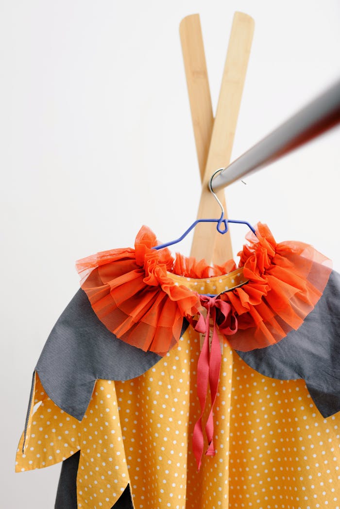 Yellow polka dot costume with vibrant collar on a wooden hanger.