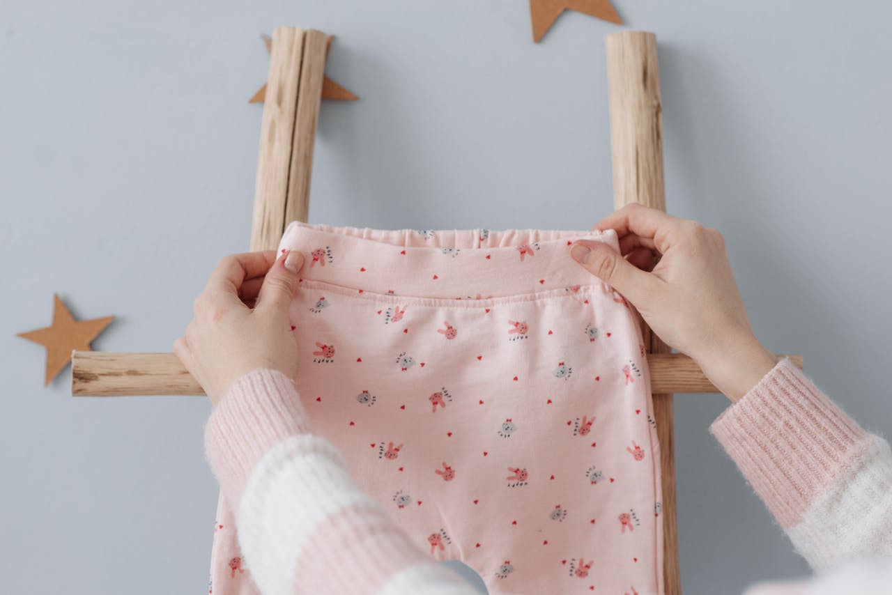 Soft pink baby trousers held on a ladder with star decorations, indoors.